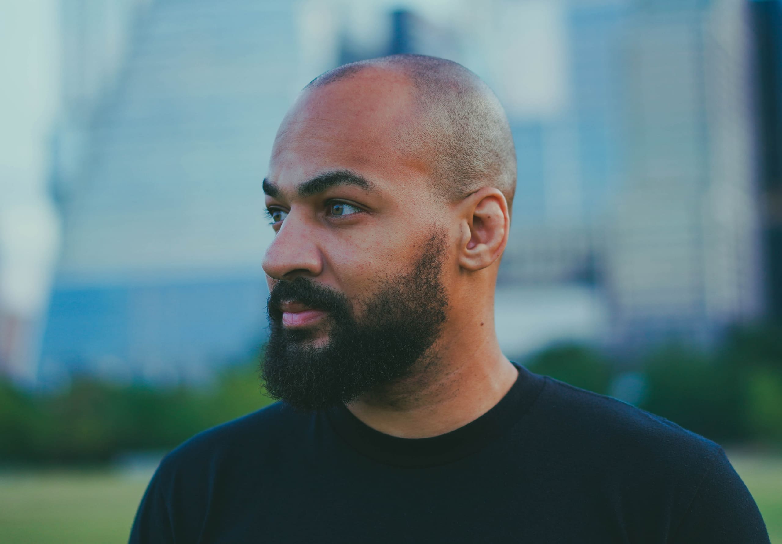 Kyle Johnson in profile, looking left, with city buildings out of focus behind him. Black and white.